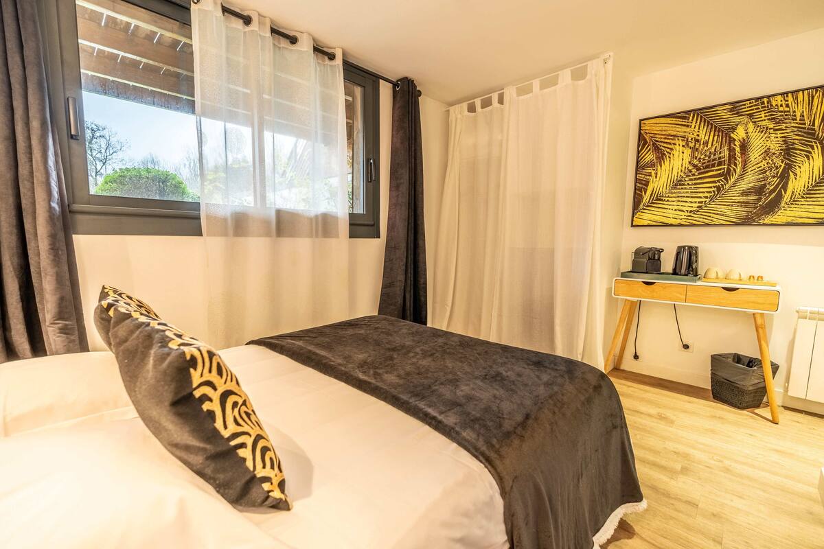 A bedroom with a bed, a desk, and a large window with curtains.