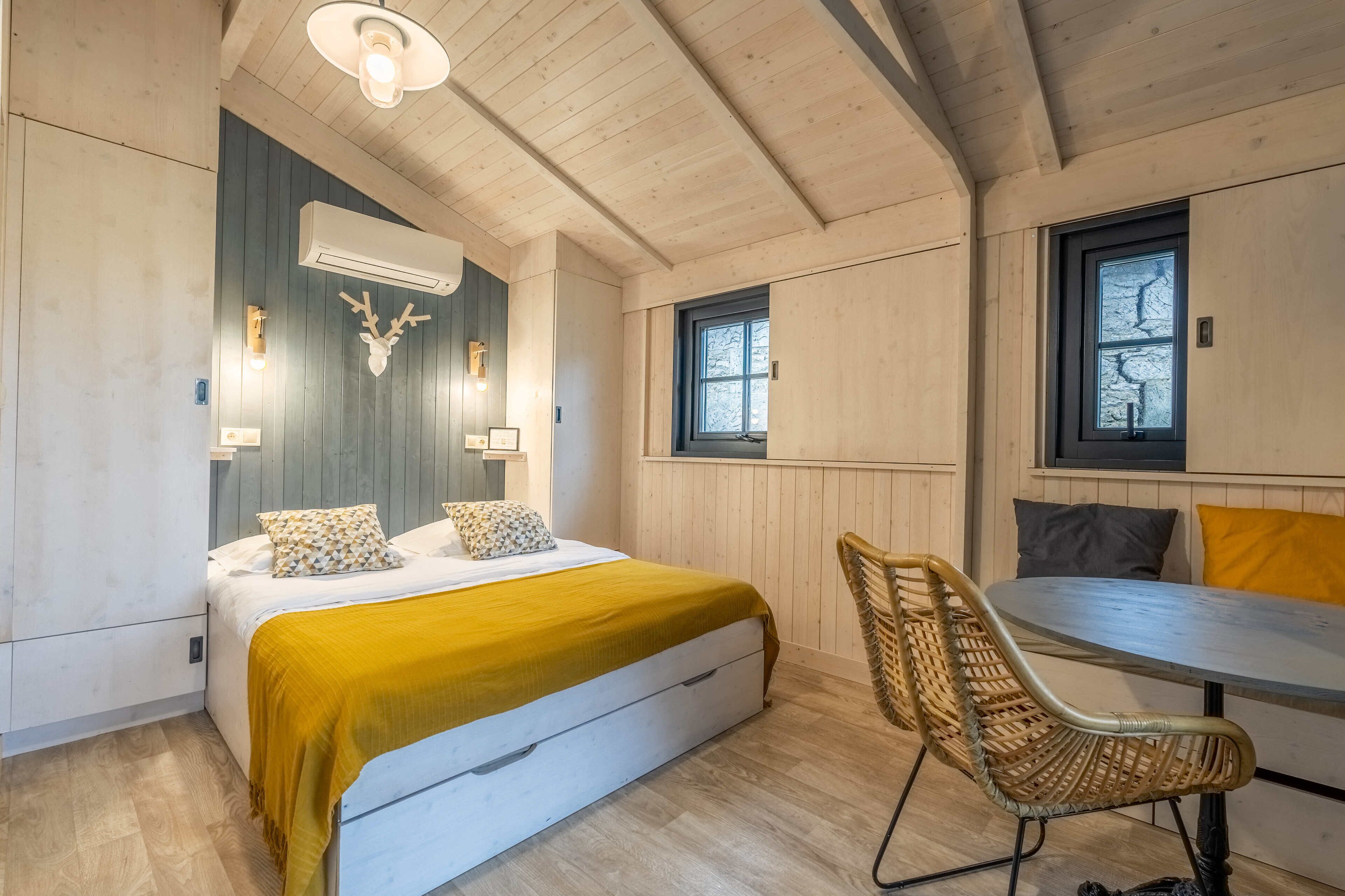 Ein gemütliches Zimmer mit einem Bett, einem Esstisch, Korbstühlen und einer Deckenleuchte.