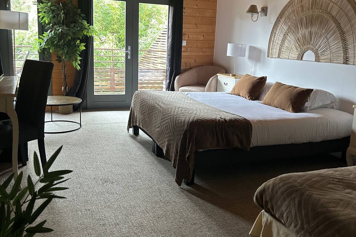 A bedroom with a bed, a desk, and a chair. There is a window with a view of greenery outside.
