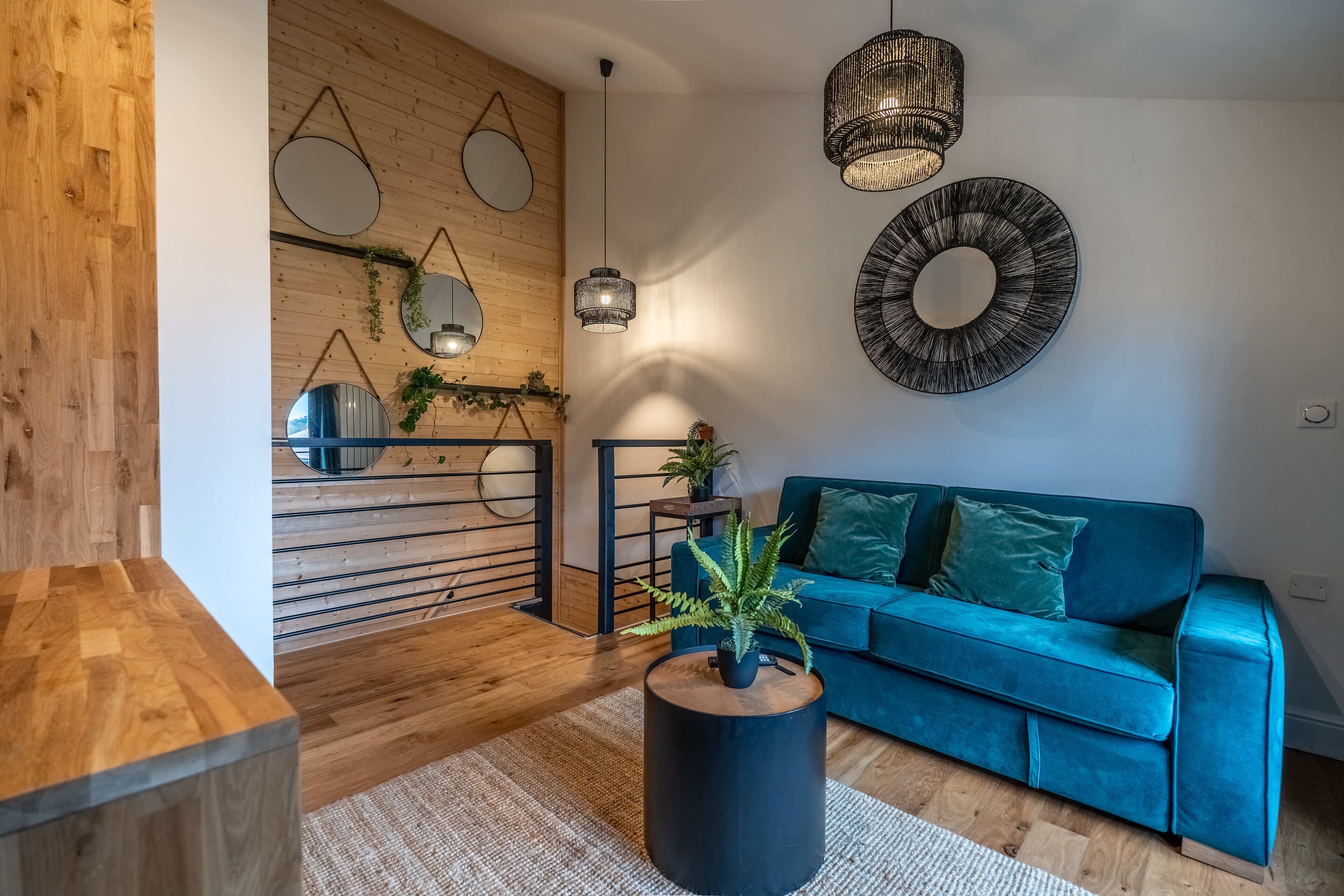 A modern living room with a wooden floor, a teal sofa, a round coffee table, and a hanging light fixture.
