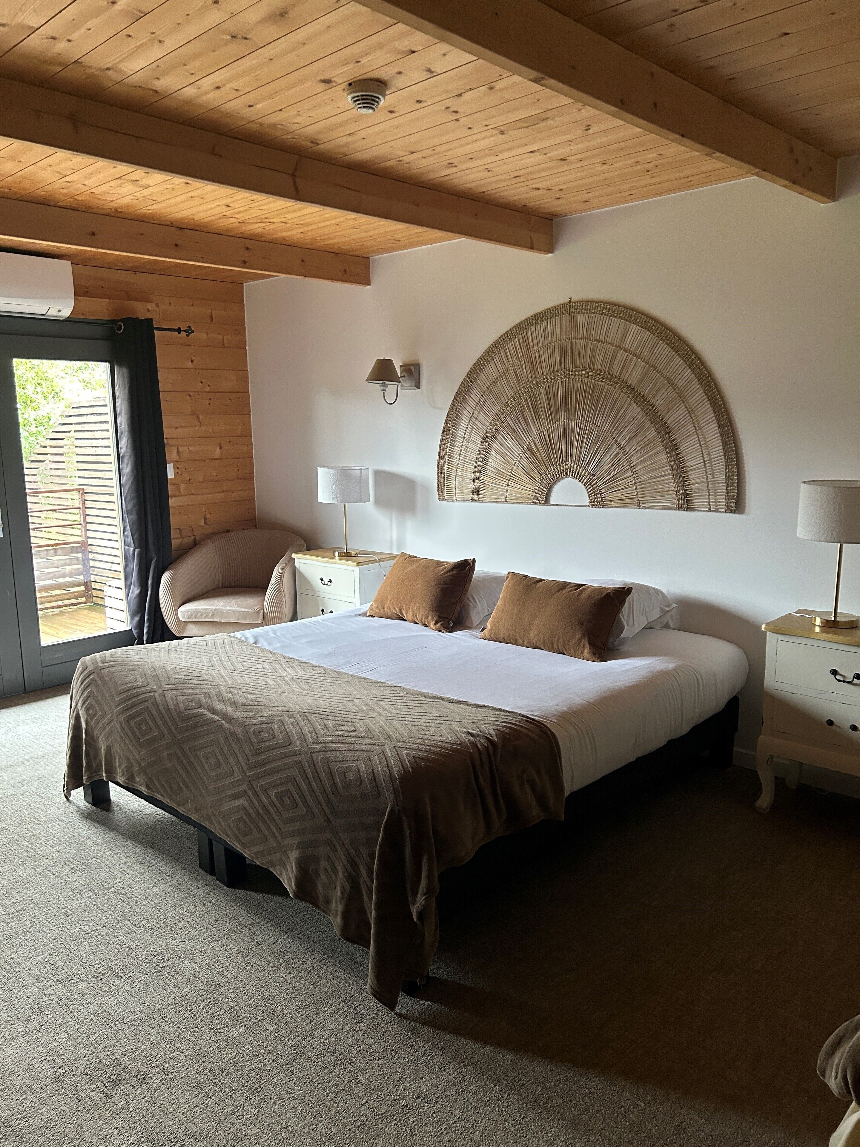 Een slaapkamer met een groot bed, een stoel, een nachtkastje en een wandlamp.