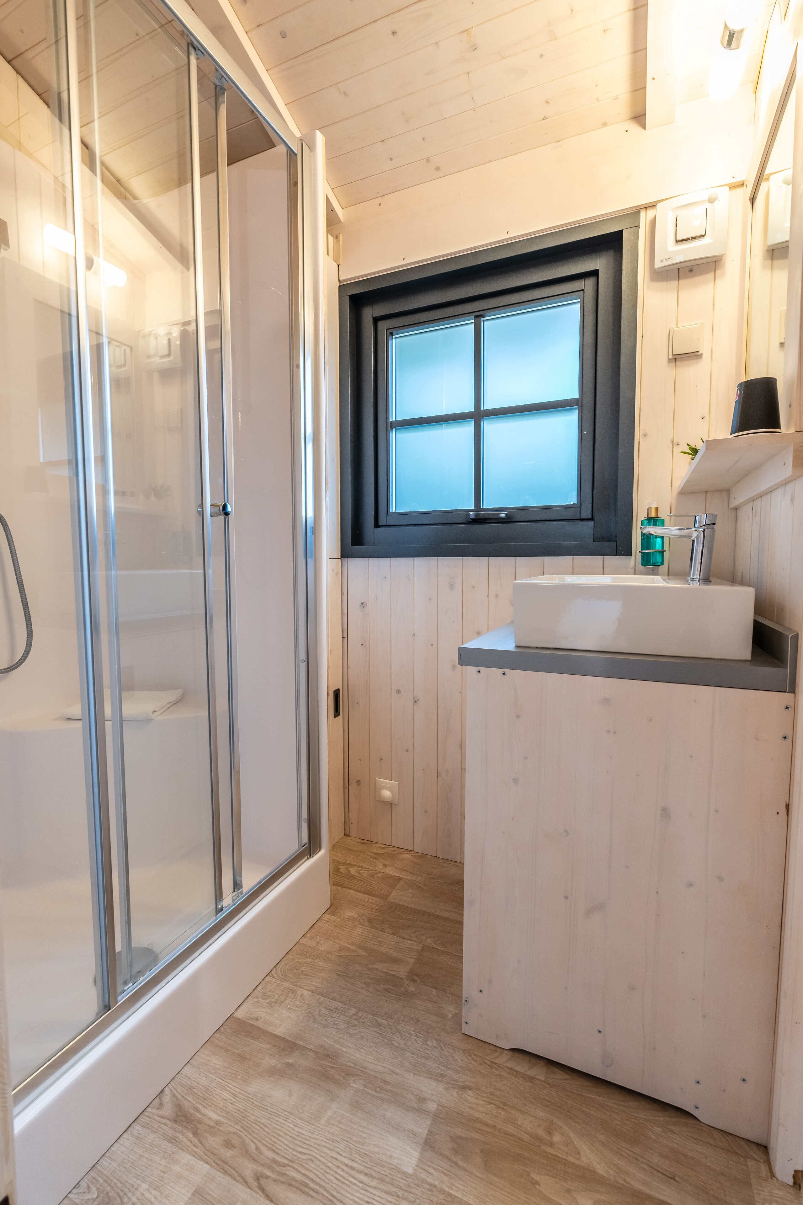 A modern bathroom with a glass shower enclosure, a wooden vanity with a sink, and a window above the sink.