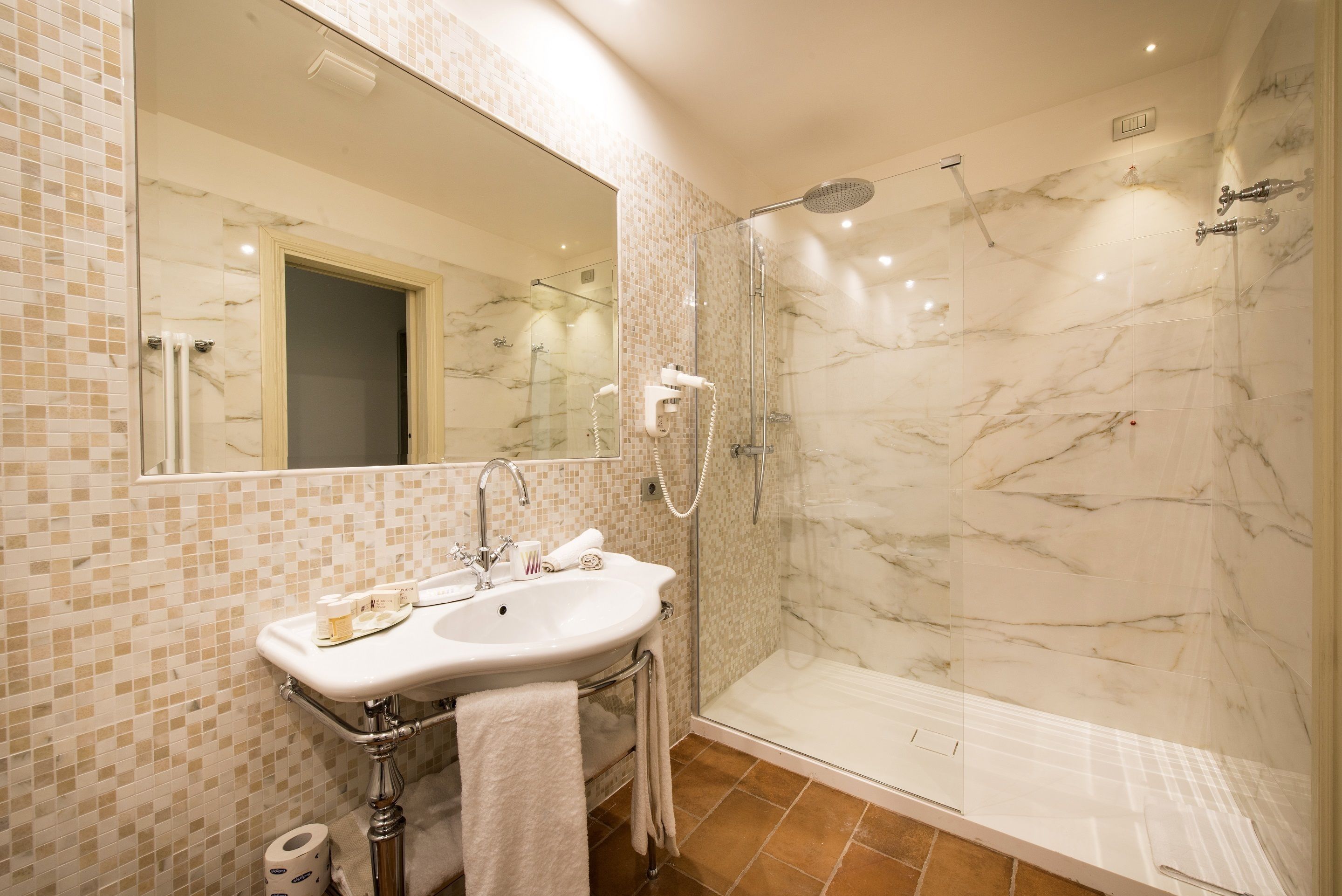 A bathroom with a marble shower, a sink with a mirror, and a tiled floor.