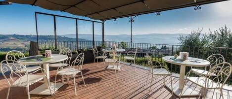 Un patio al aire libre con dos mesas redondas y sillas, una pérgola en la parte superior y una vista panorámica de colinas y montañas.
