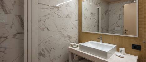 A bathroom with a marble wall, a sink with a mirror, and a shower.