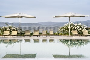 Un área junto a la piscina con sillones de descanso y sombrillas, vista despejada de las montañas y una superficie de agua tranquila que refleja el entorno.