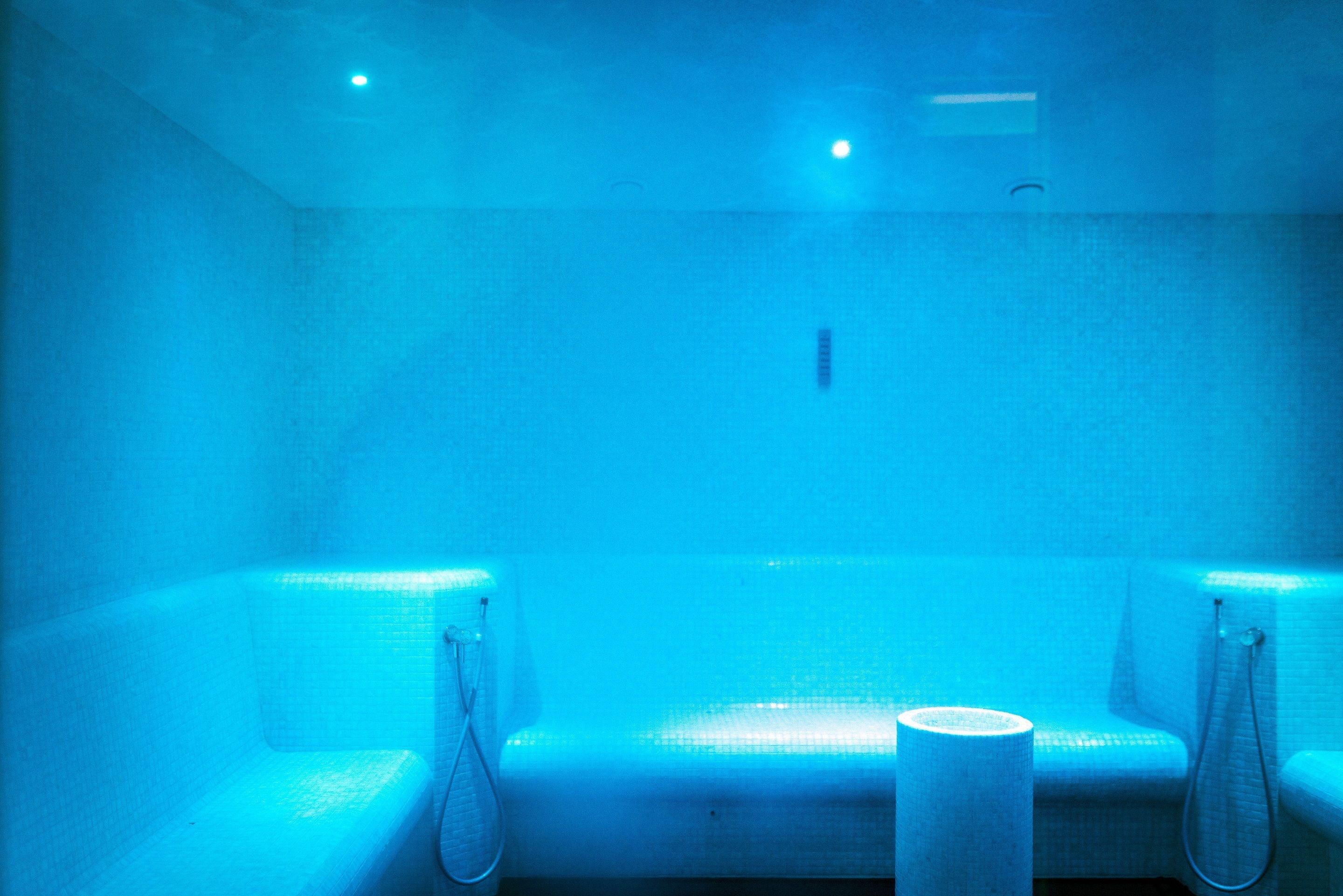 A blue-lit room with a bench and a towel rack.