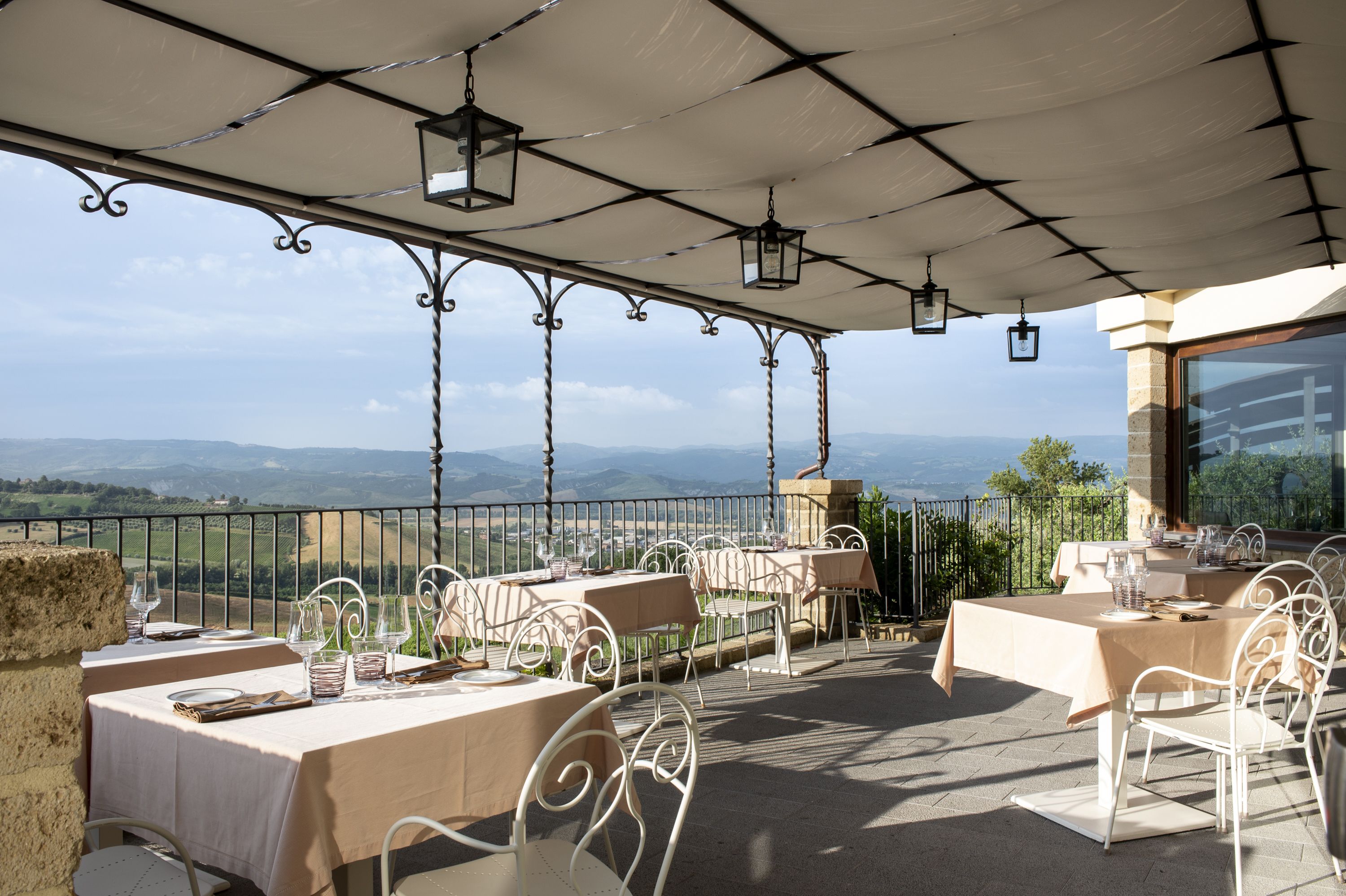 Un espace extérieur aménagé pour les repas, avec des tables et des chaises, une pergola ornée de lanternes suspendues et une vue panoramique sur la campagne.