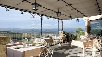 Un espace extérieur aménagé pour les repas, avec des tables et des chaises, une pergola ornée de lanternes suspendues et une vue panoramique sur la campagne.