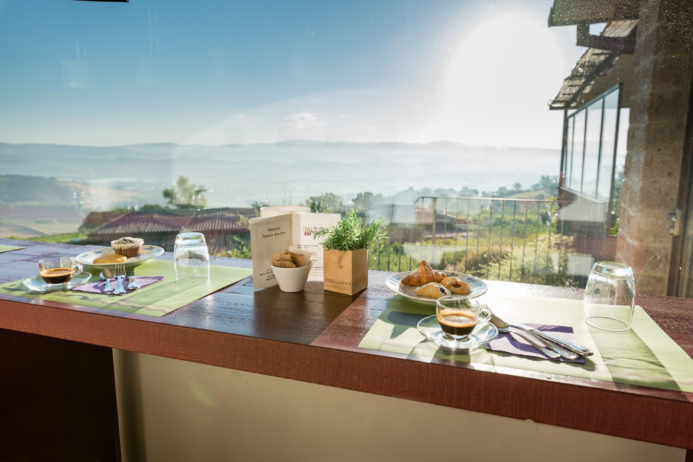 Ein Frühstückstisch mit Gebäck, Kaffee und einer Speisekarte auf einem Balkon mit Blick auf eine reizvolle Landschaft.