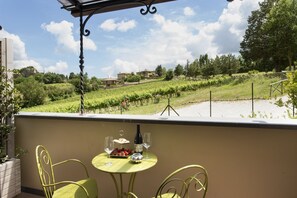Un balcón con una mesa dispuesta para dos, con vistas a un viñedo.