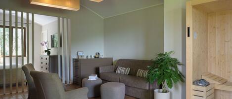 Een moderne woonkamer met een bank, fauteuils, een poef en een potplant.