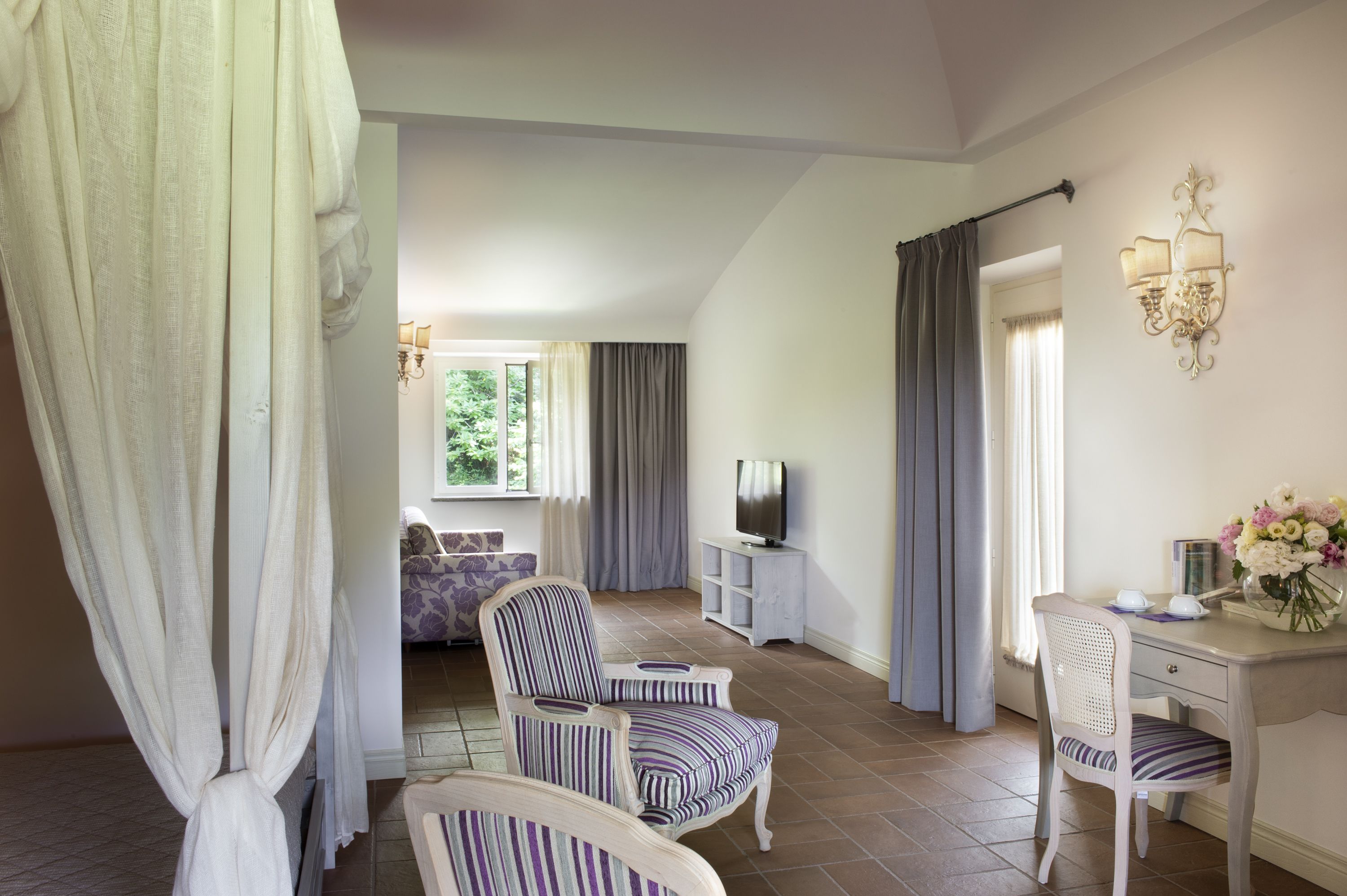 Una habitación de hotel con cama, escritorio, silla, televisor y cortinas.