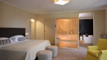 Una habitación de hotel moderna con una cama grande, una lámpara de techo brillante, una puerta de madera que da a un baño y un sillón amarillo.