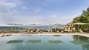 A pool with clear water, surrounded by lounge chairs and umbrellas, with a view of hills in the background. - Altarocca Wine Resort Adults Only (Orvieto)