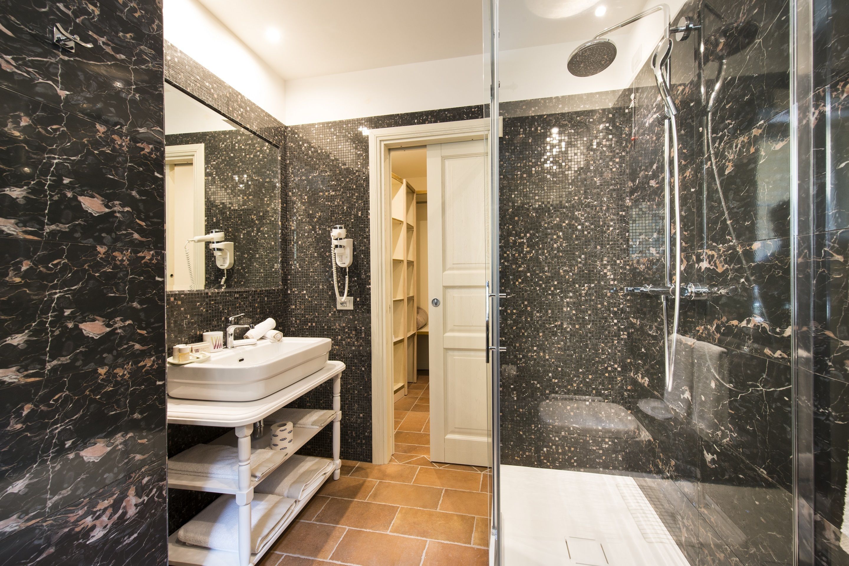 A modern bathroom with a glass-enclosed shower, a white sink, and a marble-tiled wall.