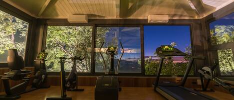 A gym with exercise equipment, large windows, and a view of a canyon at dusk.