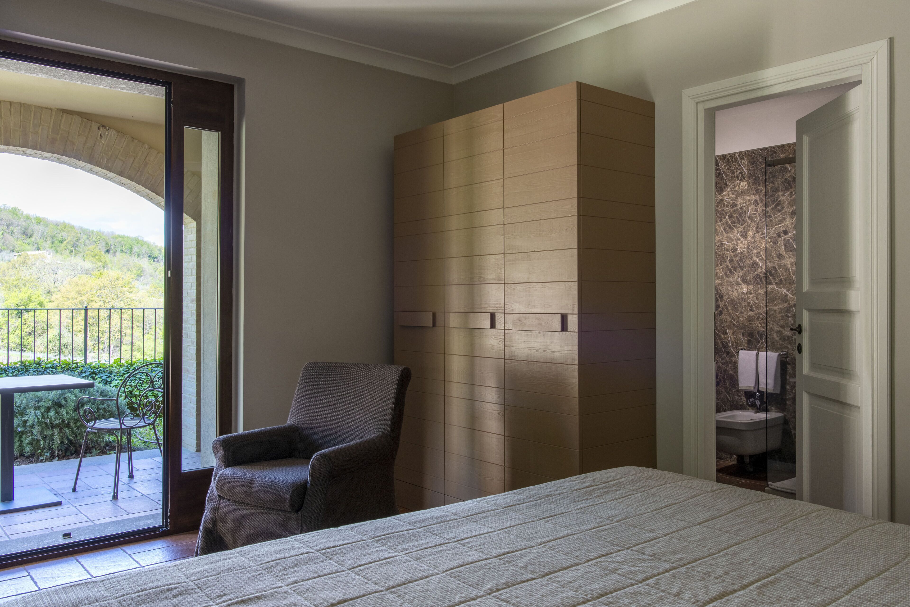 Un dormitorio con cama, una silla y vistas a un balcón con mesa y sillón.