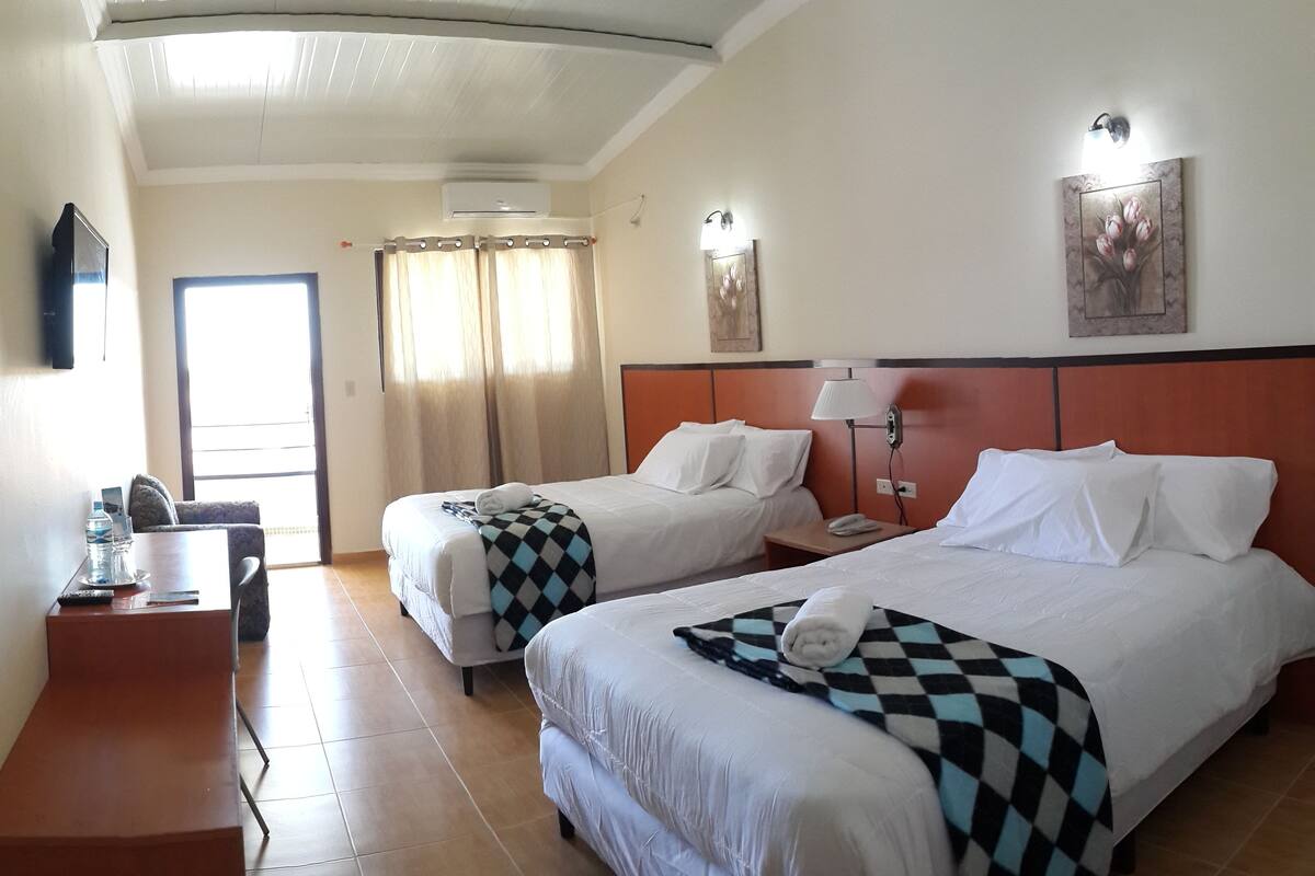A hotel room with two beds, a desk, a chair, a TV, and a window with curtains.