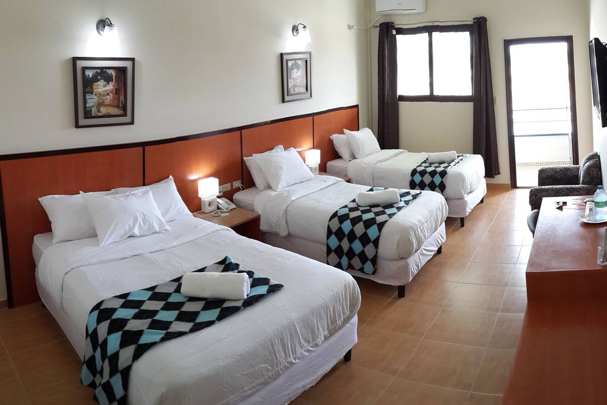 A hotel room with three beds, a desk, and a chair.