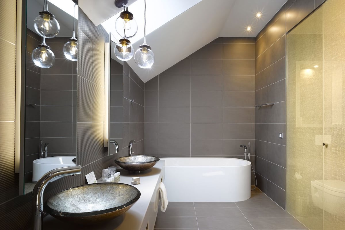 A modern bathroom with a freestanding bathtub, two sinks with large bowls, and a skylight.
