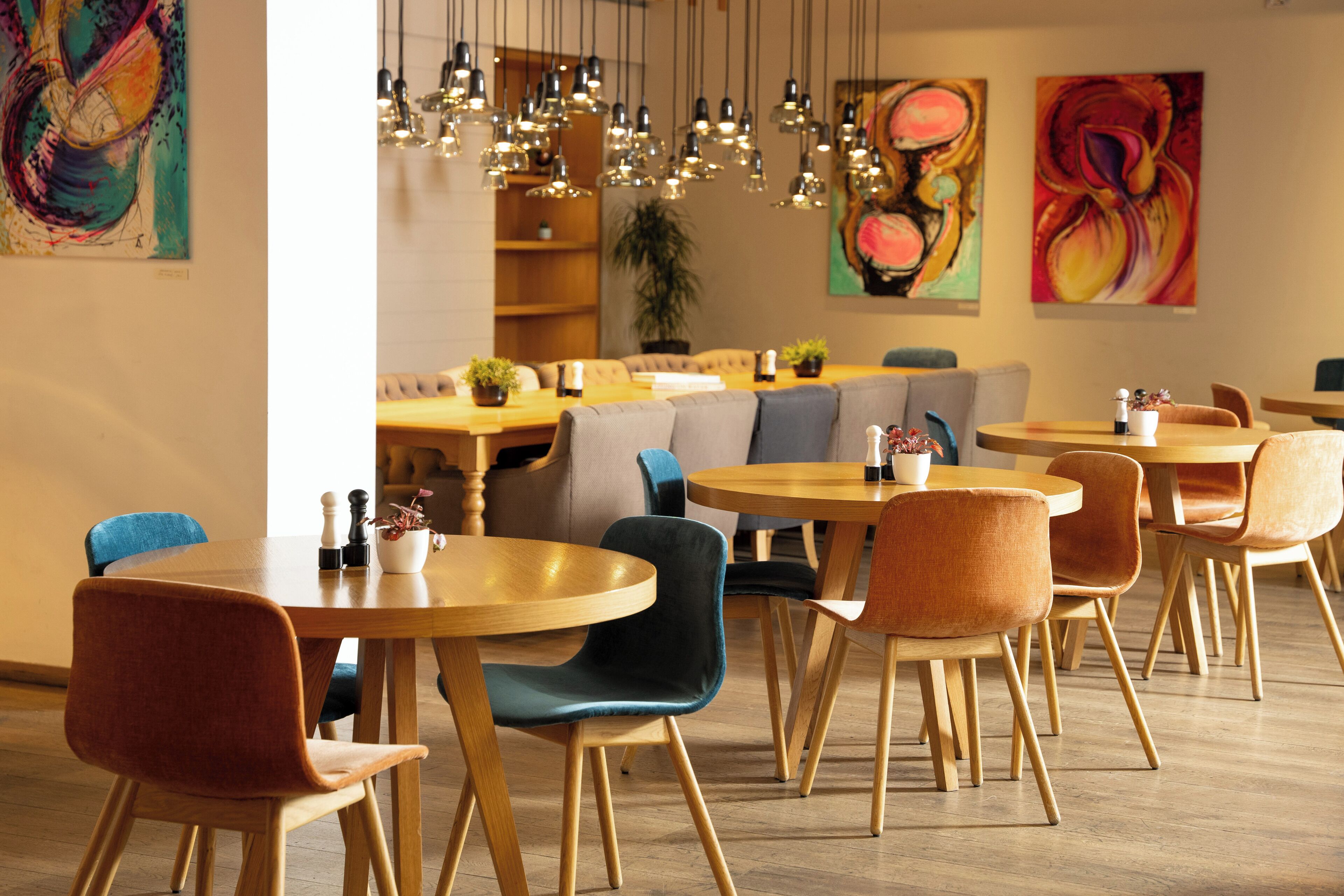 A modern dining area with round tables and chairs, wooden floors, and hanging pendant lights.