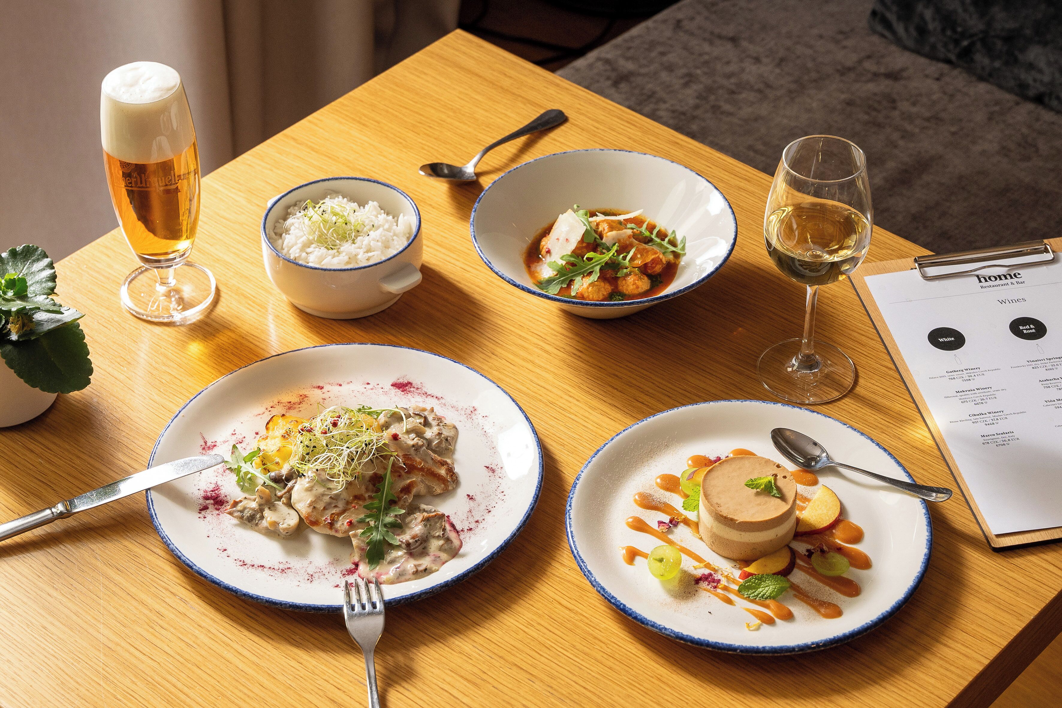 A wooden table with a menu, a glass of beer, bowls of rice and soup, and plates of food.