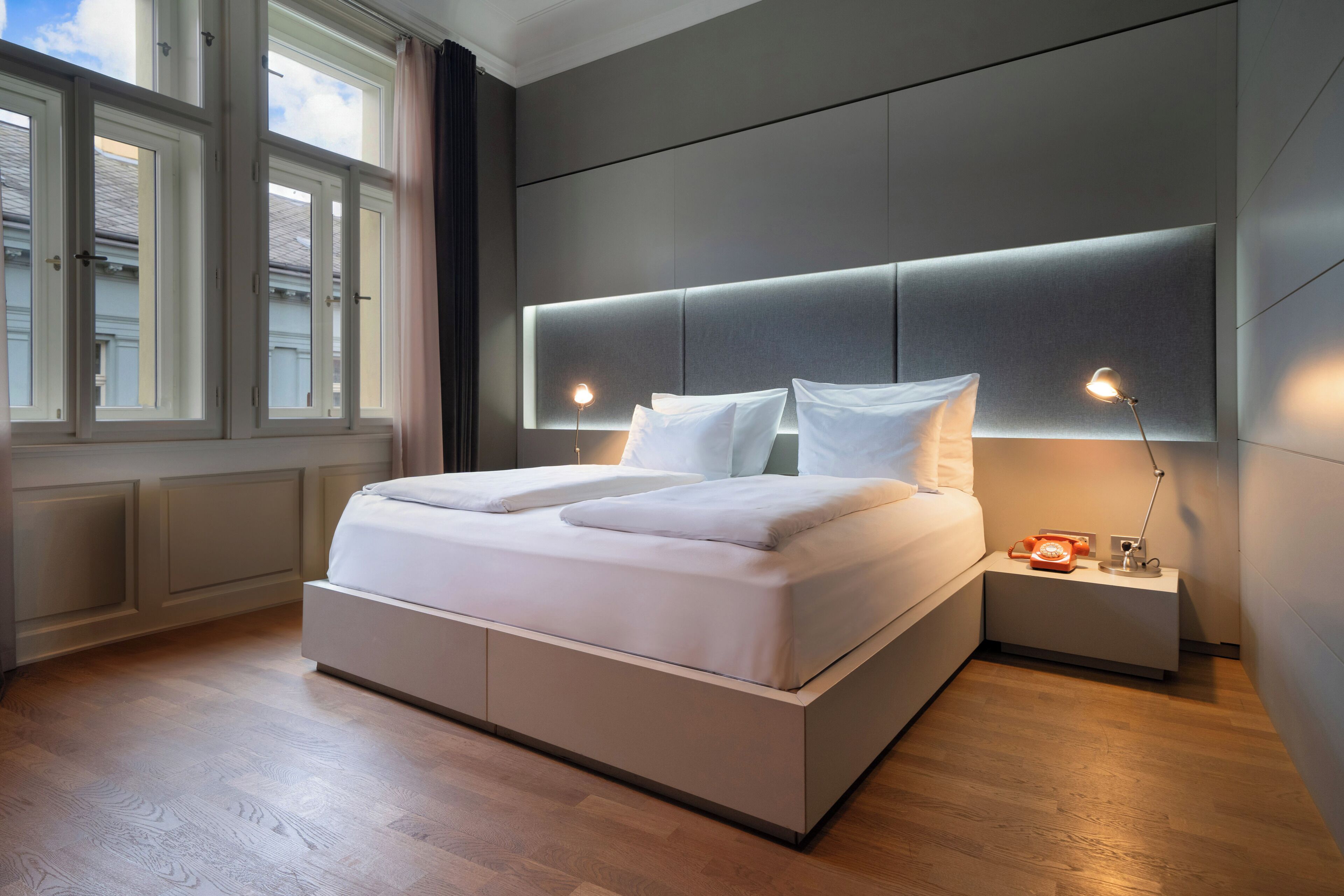 Un dormitorio moderno con una cama grande, lámparas de noche y vistas amplias a través de ventanas grandes.