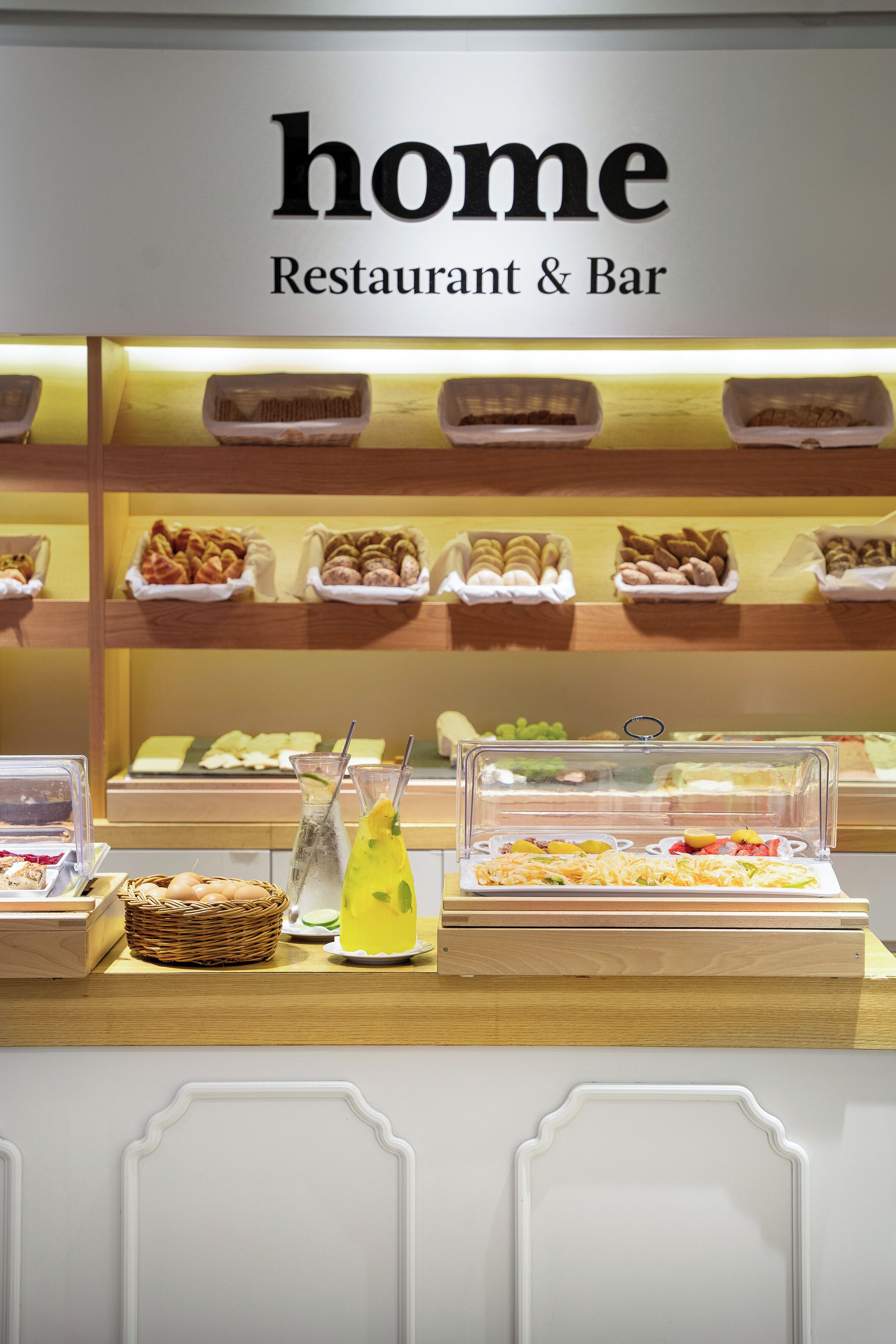 Espaço de buffet de café da manhã com diversos alimentos e um letreiro que diz 'home Restaurant & Bar'.