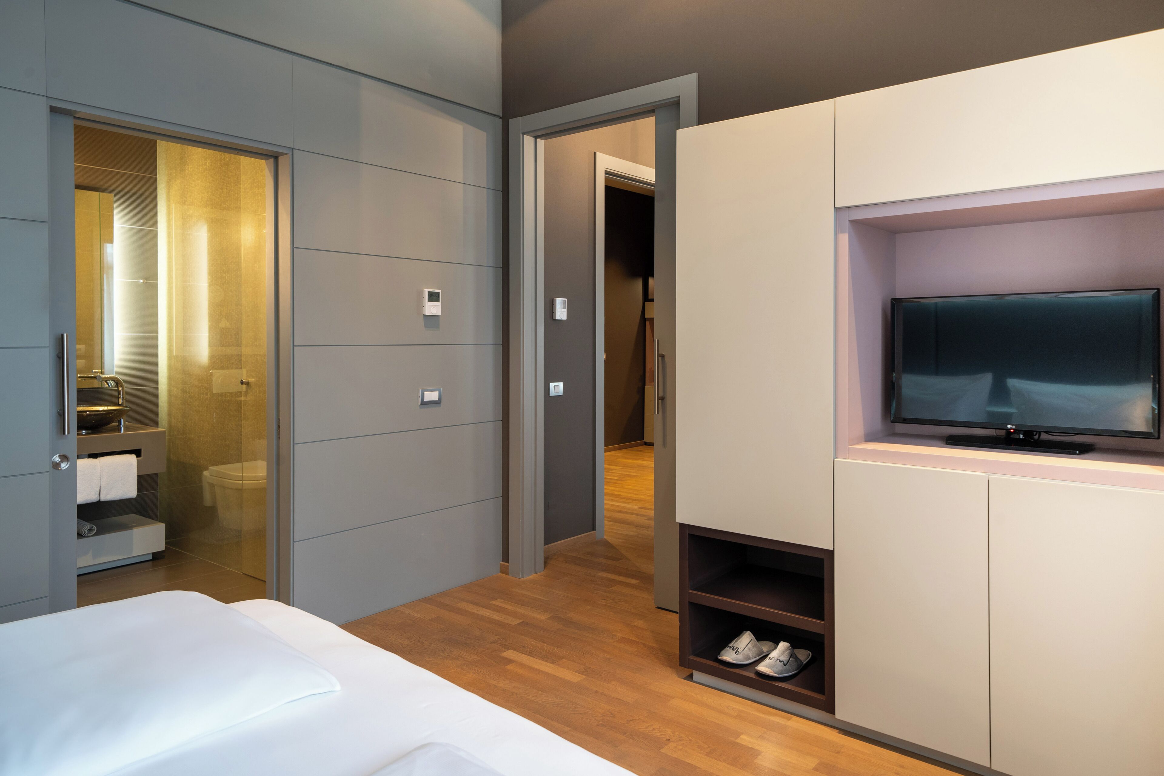 Una habitación de hotel moderna con una cama, televisión y vestidor.