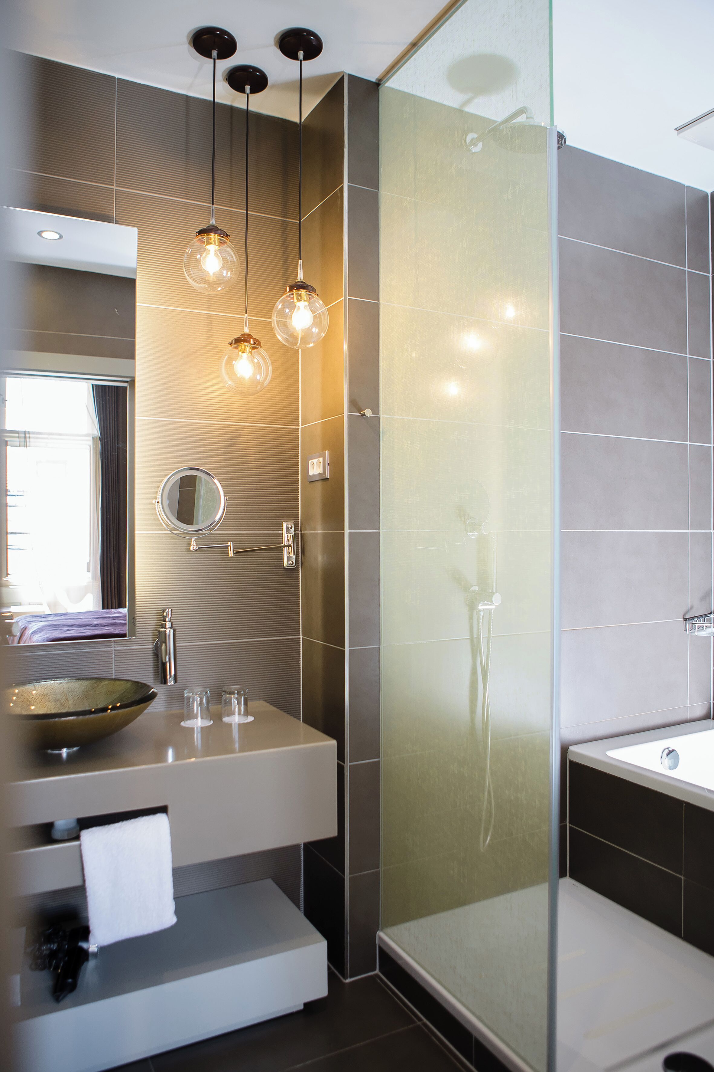 A modern bathroom with a glass-enclosed shower, a vanity with a bowl sink, and pendant lighting.