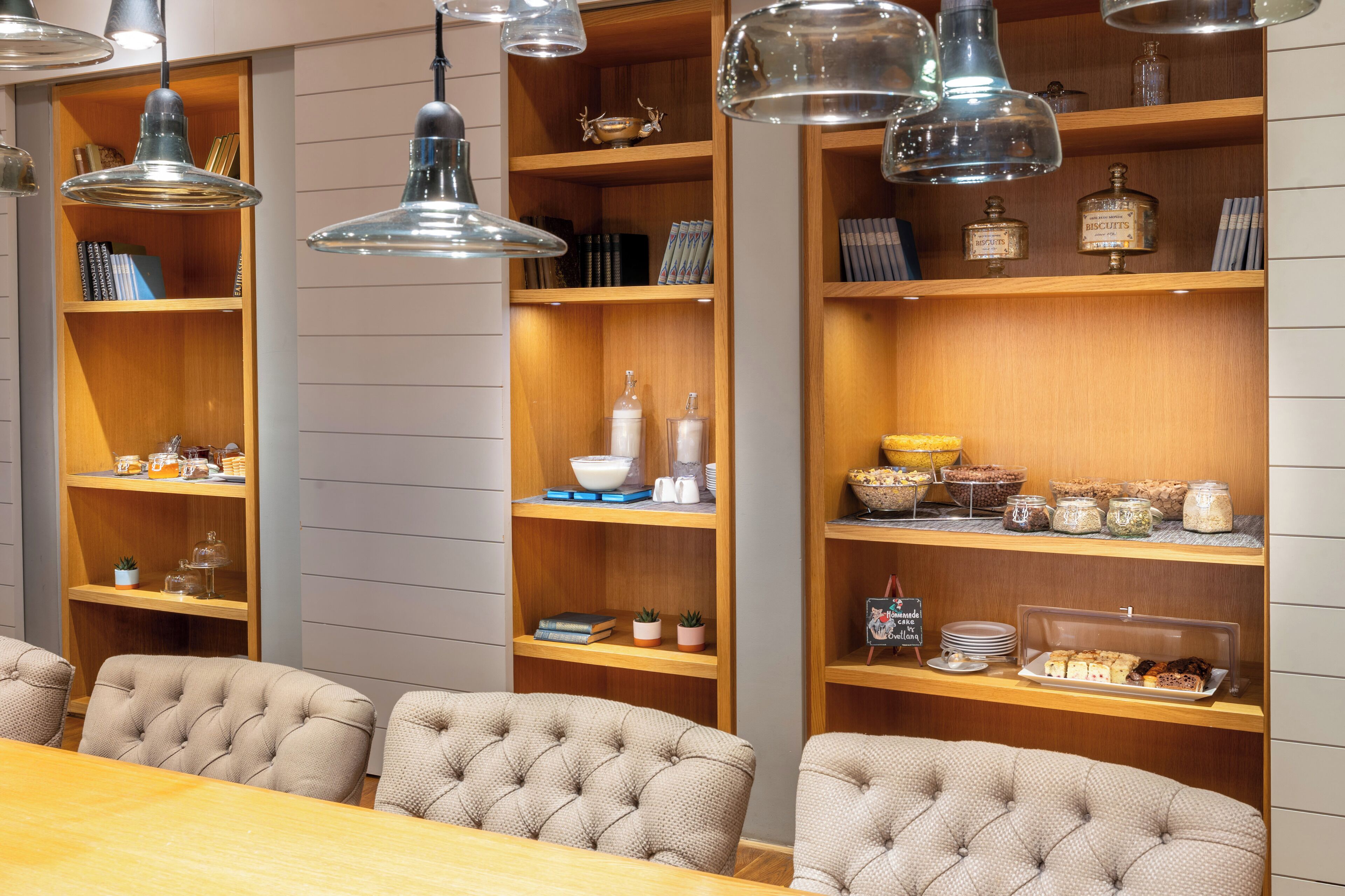 Un espace repas avec une table en bois et des chaises à capitonnage, entouré d’étagères où sont exposés des livres, des objets décoratifs et des produits alimentaires.