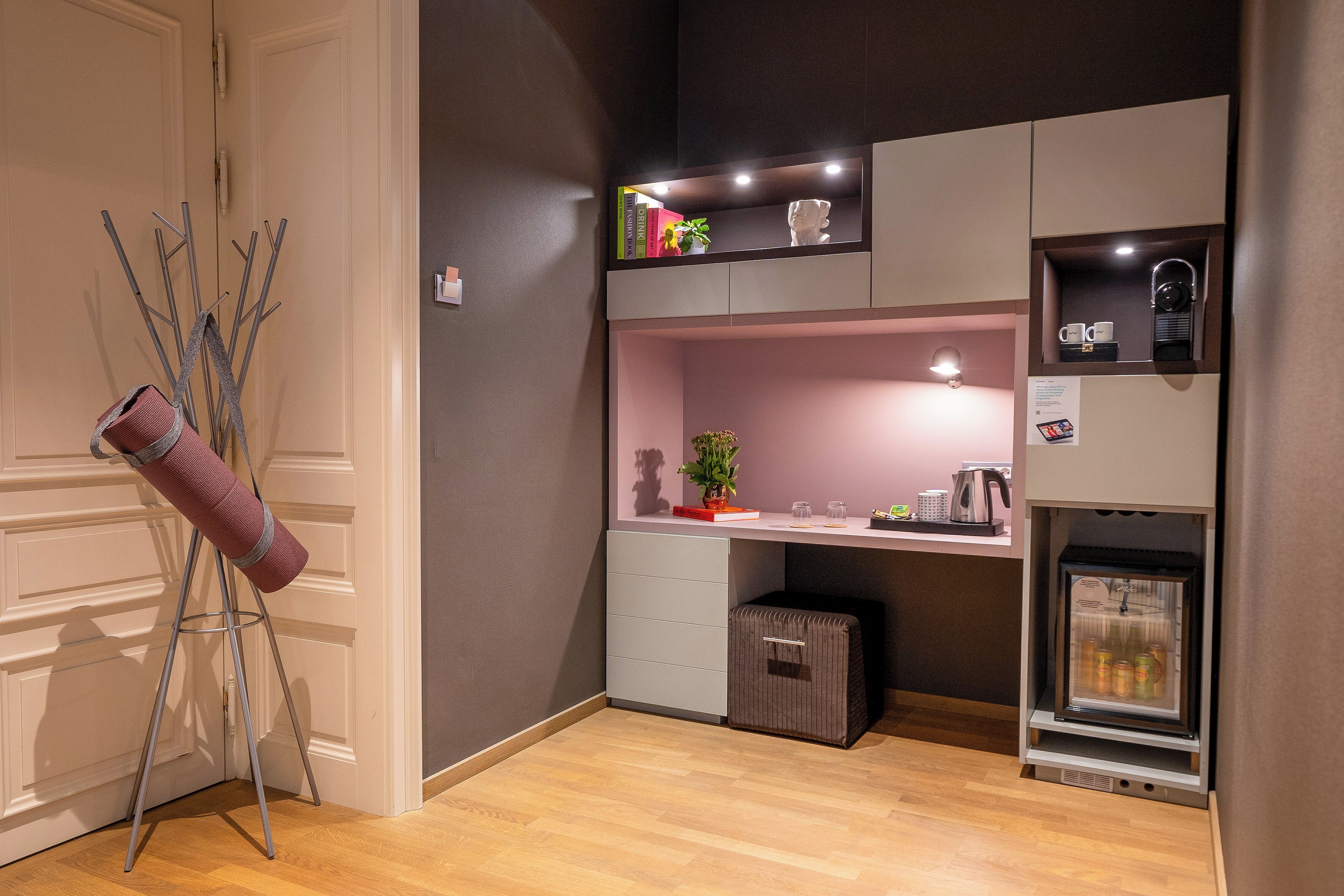A compact kitchenette with a built-in coffee machine, a mini-fridge, and a small countertop with a potted plant.