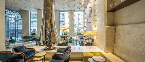 A spacious lobby with a large central column, seating areas, and a view of the city through large windows.