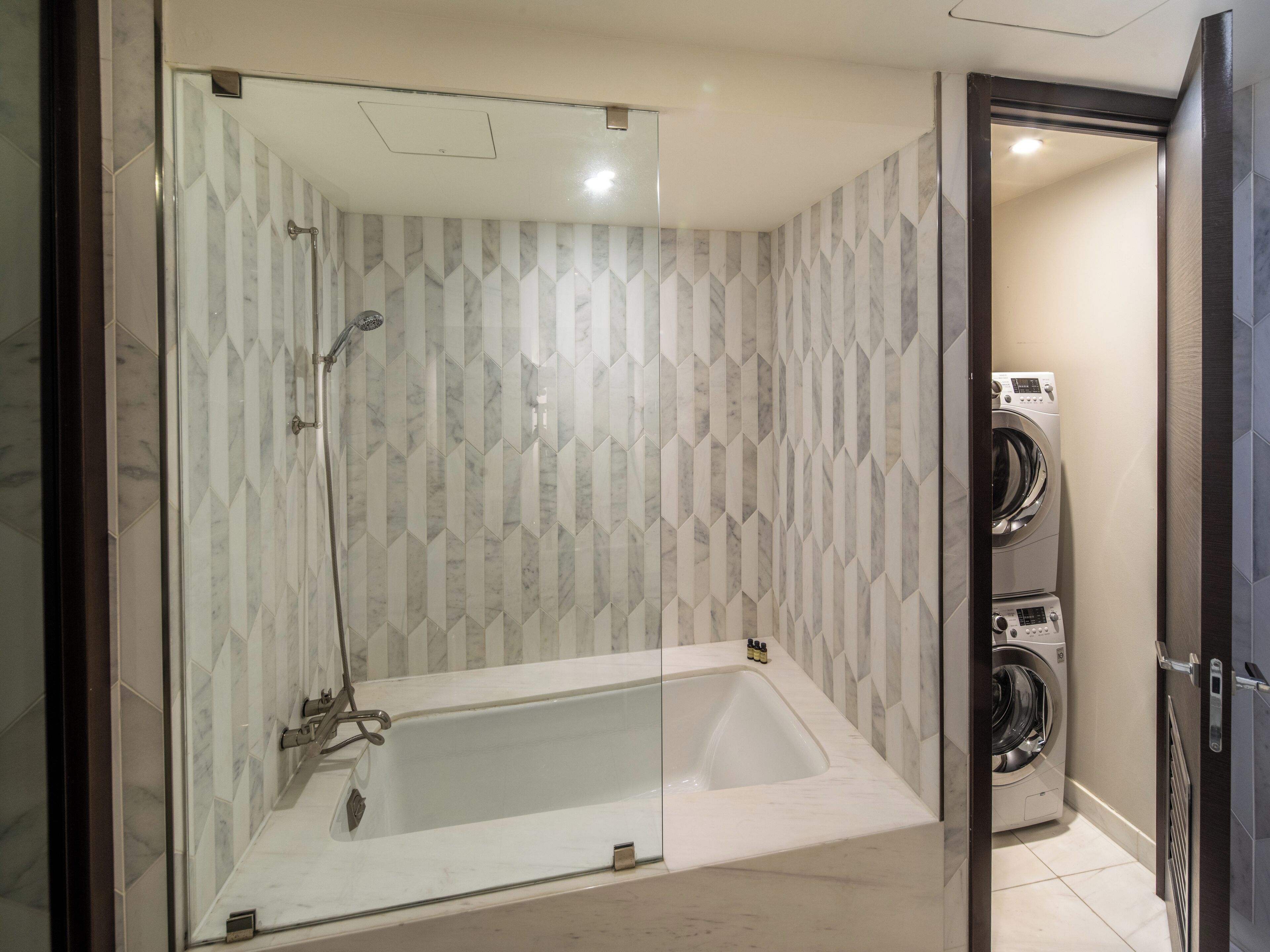 Een moderne badkamer met een douchecabine van glas, een witte badkuip en een ingebouwde wasmachine.