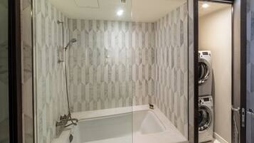Een moderne badkamer met een douchecabine van glas, een witte badkuip en een ingebouwde wasmachine.
