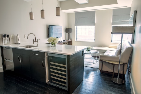 A modern kitchen with a central island, black cabinets, and stainless steel appliances. There is a dining area with a white sofa and a small round table. - The Marmara Park Avenue (New York)