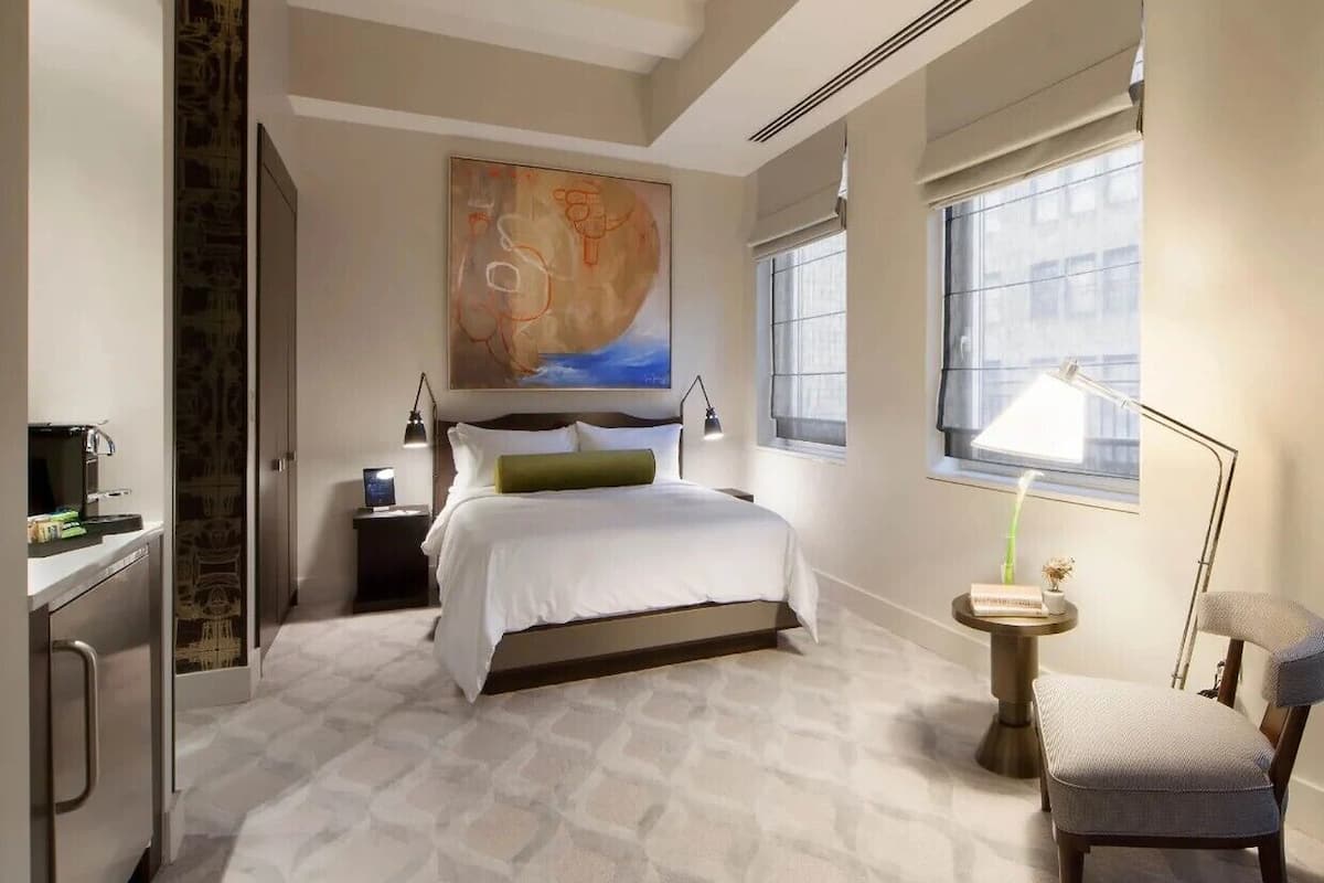 Una habitación de hotel moderna con una cama grande, un escritorio con computadora, una silla y una ventana con vistas a la ciudad.