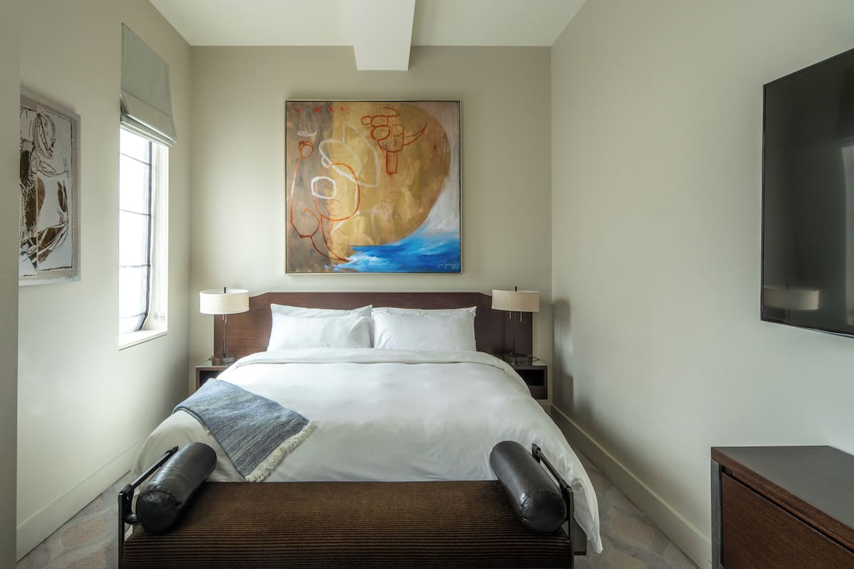 Una habitación de hotel con una cama grande, dos mesitas de noche, un televisor de pared y un cuadro sobre la cama.