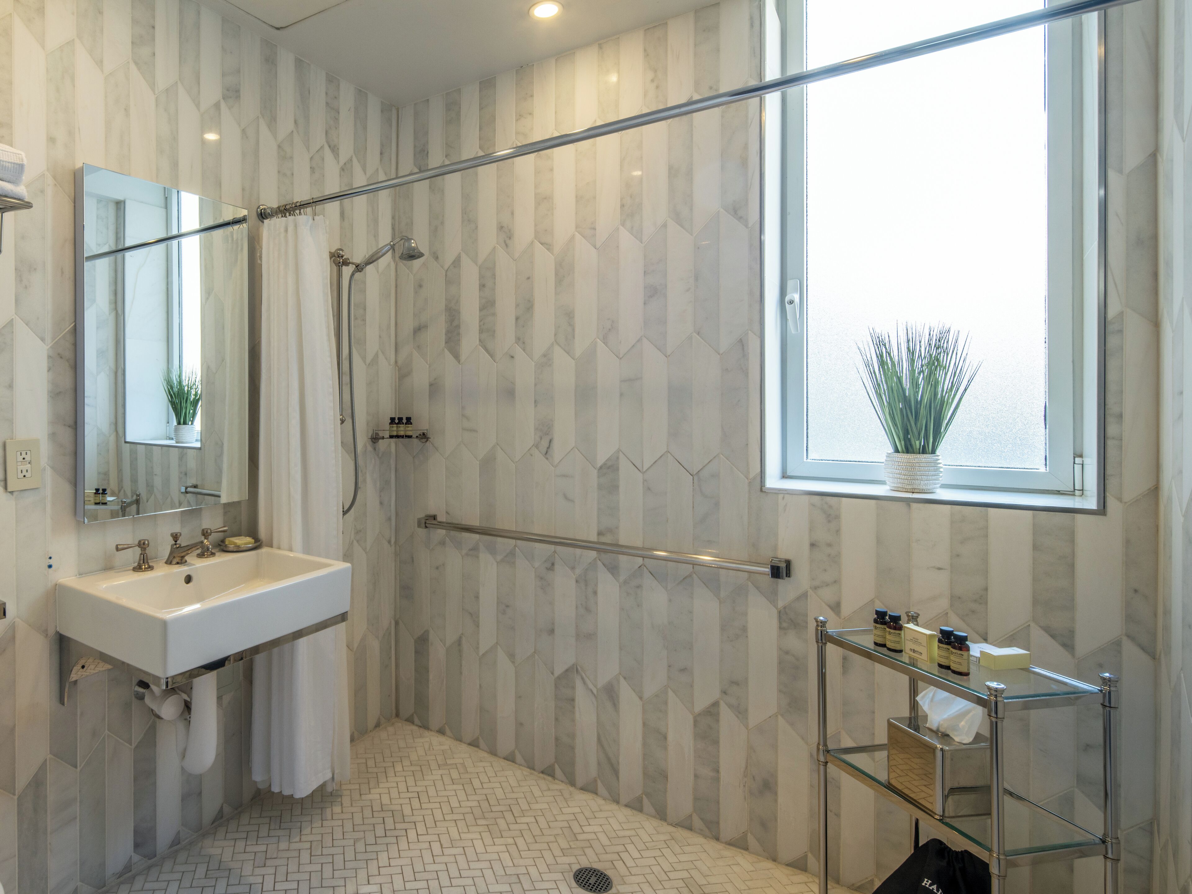 A modern bathroom with a shower, a sink, and a window with a plant.