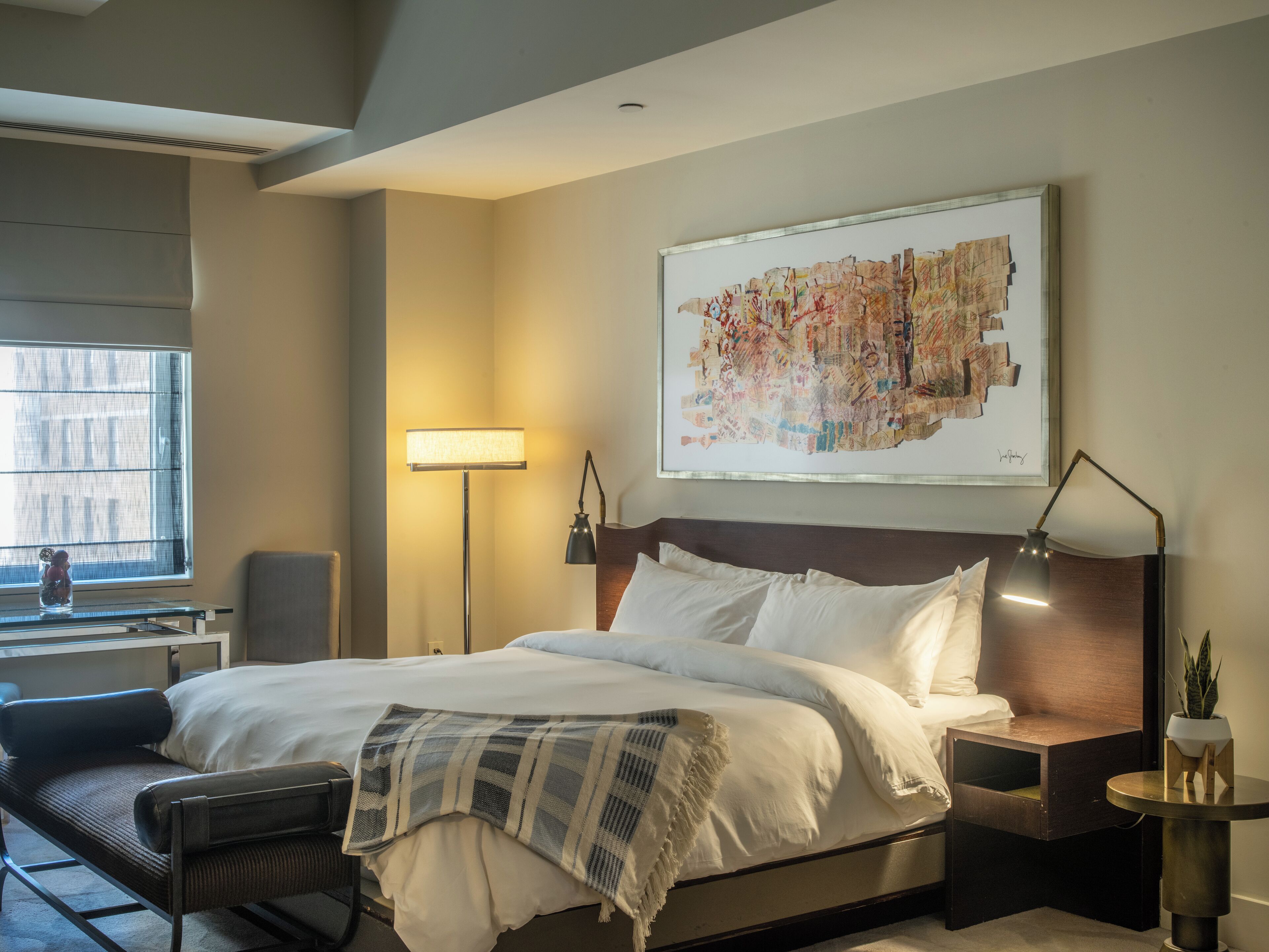 A hotel room with a large bed, bedside tables, a desk, a chair, a lamp, and a window.