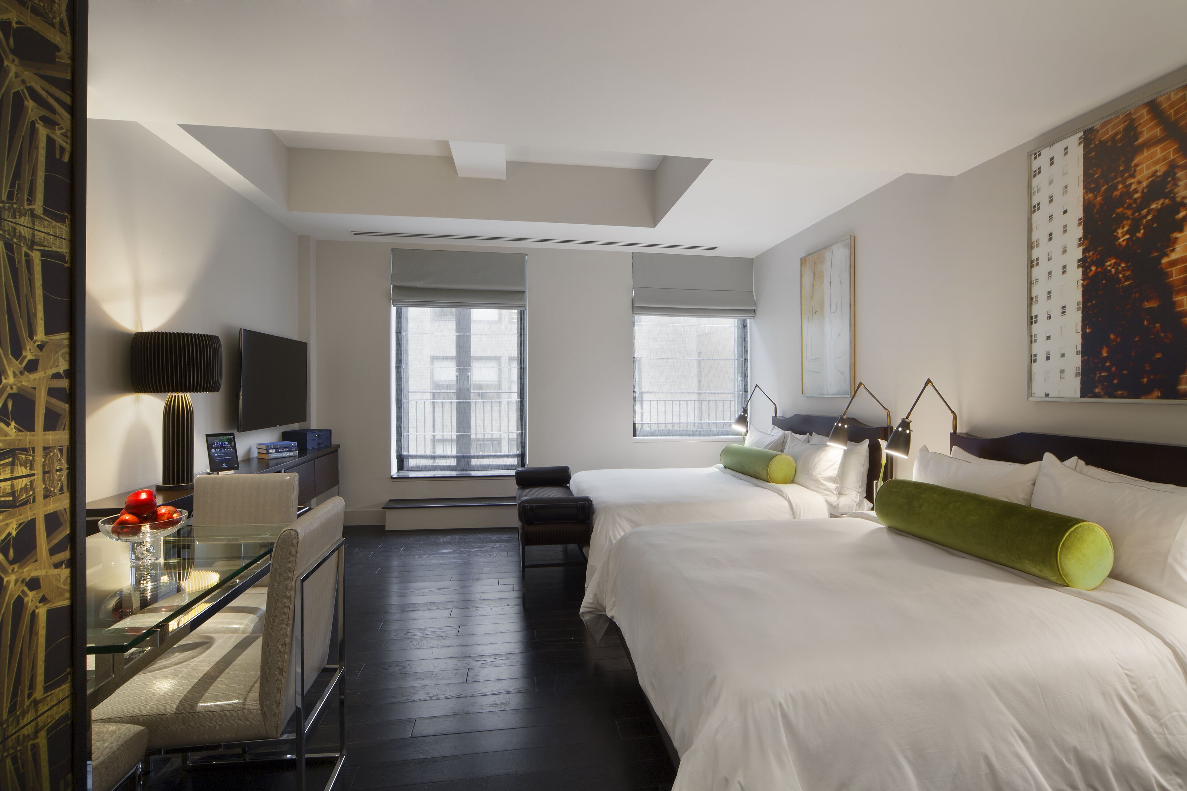 A hotel room with a bed, a desk with a computer, a chair, and a window with blinds.