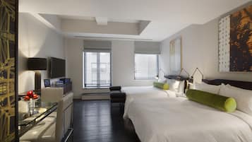 A hotel room with a bed, a desk with a computer, a chair, and a window with blinds.