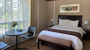 A hotel room with a bed, bedside tables, a chair, a small table, and a window with curtains.