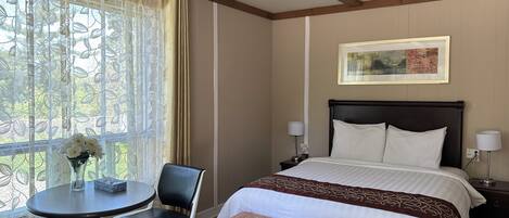 Habitación de hotel con cama, mesitas de noche, una silla, una pequeña mesa y una ventana con cortinas.