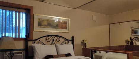 A hotel room with a bed, a bedside table with a lamp, a mirror, and a framed picture on the wall.