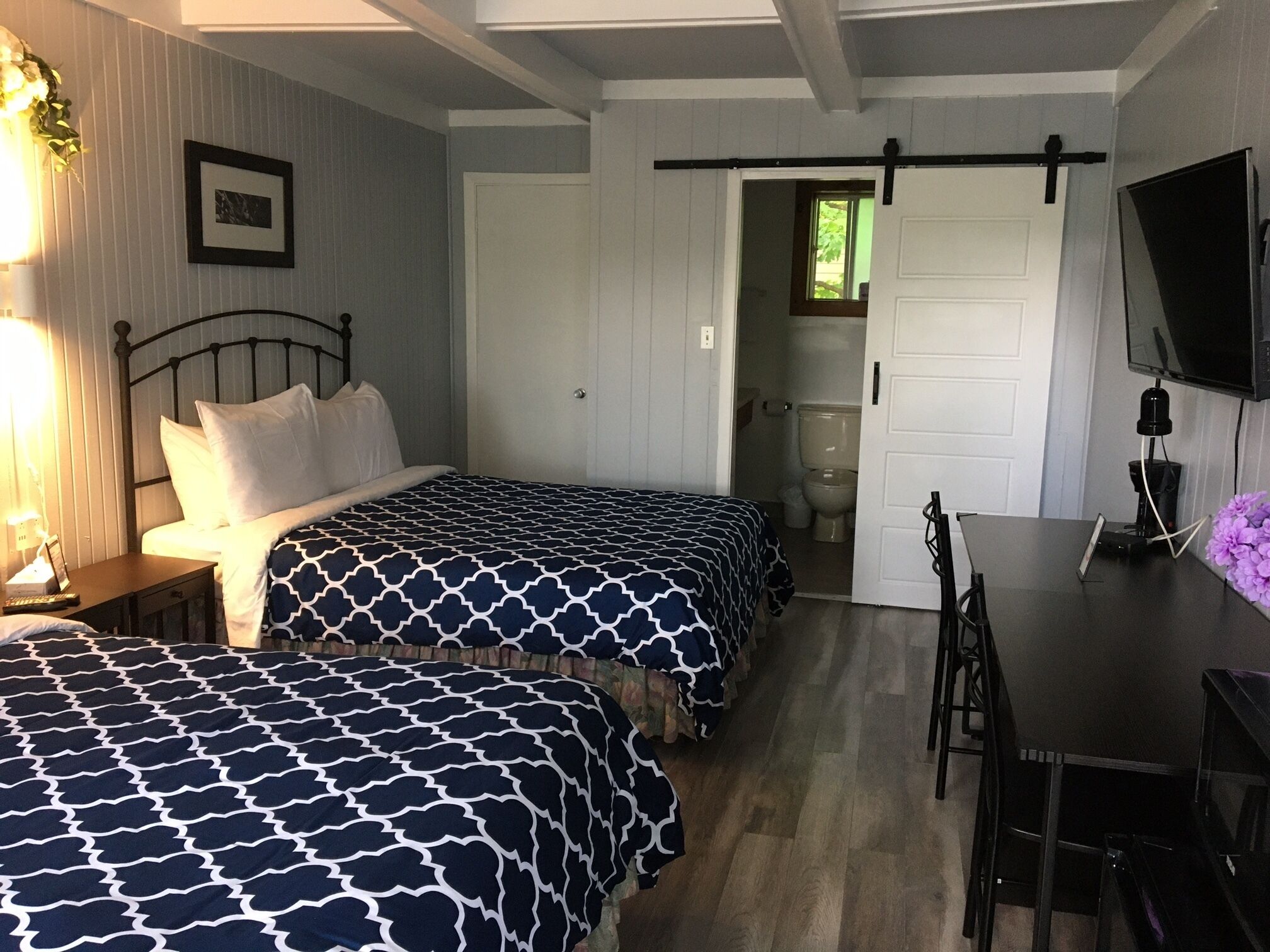 Une chambre avec deux lits, une table, un téléviseur et une porte donnant sur une salle de bain.