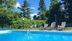 A swimming pool with lounge chairs and a small table, surrounded by trees and greenery.