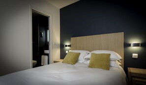 A hotel room with a bed, two bedside tables, a nightstand, a wooden headboard, and two wall-mounted lights. - Hotel Mirabeau Eiffel (Paris)