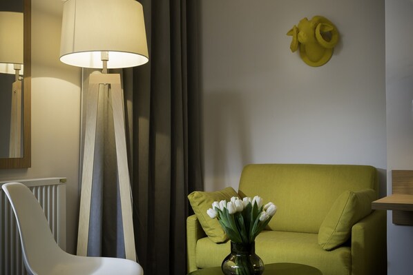 Uma sala de estar moderna com um sofá verde, uma cadeira branca e um vaso com flores brancas.
